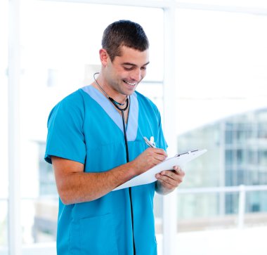 Concentrated male doctor making notes in a patient's folder clipart