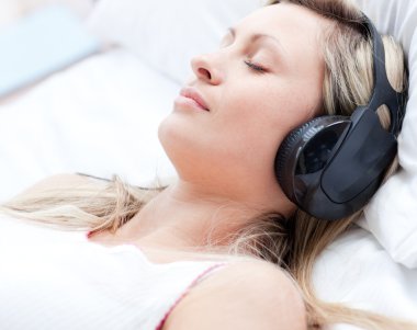 Attractive woman with headphones on sleeping on a bed clipart