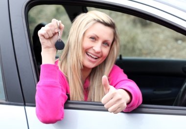 Happy female driver showing a key after bying a new car clipart