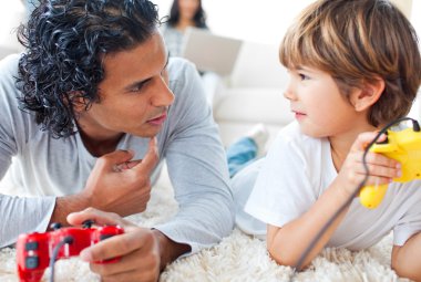 Father and his little boy playing video games lying on the floor clipart