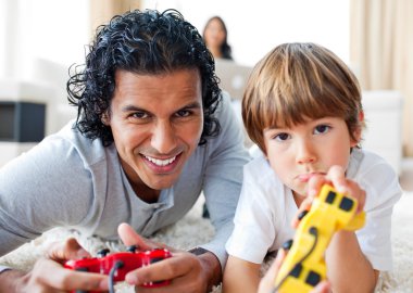 Happy father and his son playing video games lying on the floor clipart