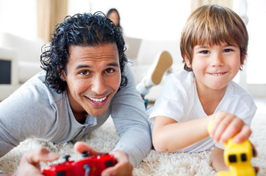 Cheerful father and his son playing video games lying on the flo clipart