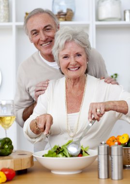 Happy senior couple eeating a salad in the kitchen clipart