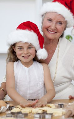 Smiling grandmother and little girl baking Christmas cakes clipart