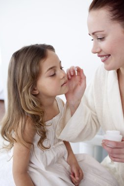 Mother putting cream on her daughter's face clipart