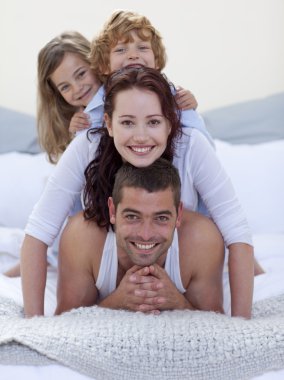 Portrait of happy parents and children having fun in bed clipart