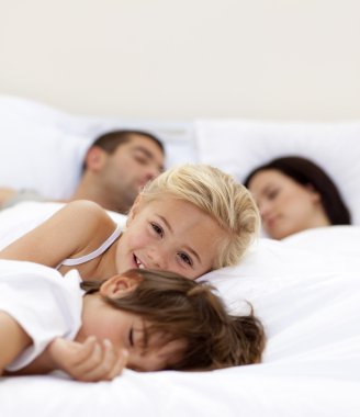 Little girl smiling wile her parents and brother sleep clipart