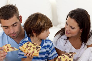 Prents and son eating pizza in living-room clipart