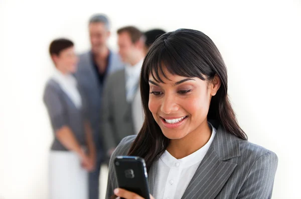 Smiling businesswoman sending a text in front of her team — Stock Photo, Image