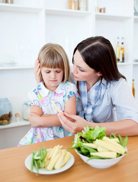 Ontevreden blond meisje eten van groenten met haar moeder — Stockfoto