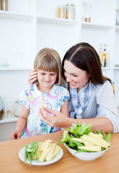 Smiling little girl eating vegetables with her mother — Stock Photo, Image