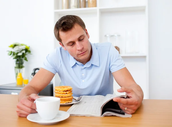 stock image Concentrated man reading a newspaper while having breakfast