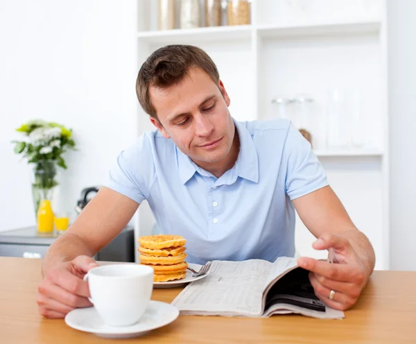 Sorrindo homem lendo um jornal enquanto toma café da manhã — Fotografia de Stock