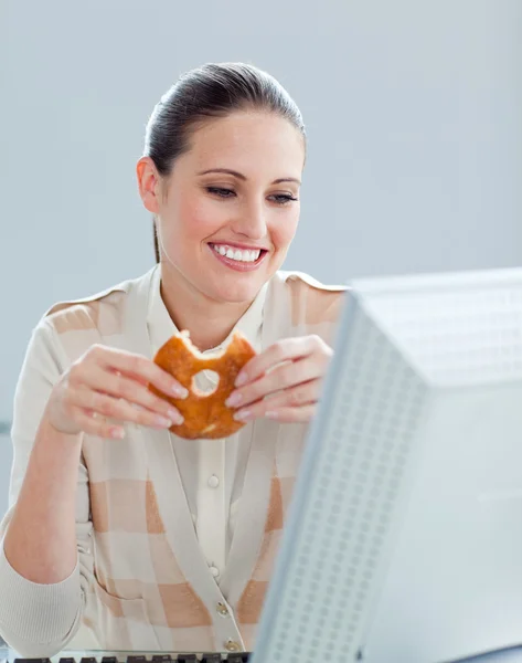 Портрет кавказской деловой женщины, поедающей пончики в своем офисе — стоковое фото