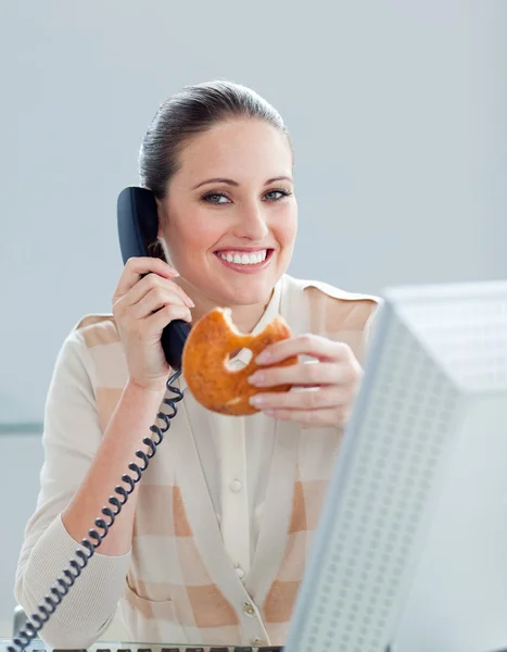 Positive businesswoman on phone eating a donnut — Stock Photo, Image