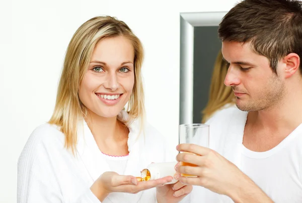 Mulher bonita segurando pílulas e homem bebendo suco de laranja — Fotografia de Stock