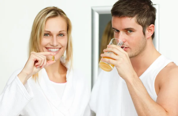 Woman holding pills and man drinking orange juice — Stock Photo, Image