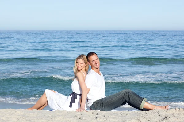 Uśmiechający się para siedzi na piasku — Zdjęcie stockowe