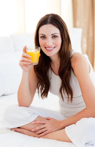 ブルネットの女性がベッドの上にオレンジ ジュースを飲む — ストック写真