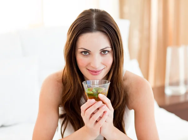 Portret van een jonge vrouw drinken thee zittend op bed — Stockfoto