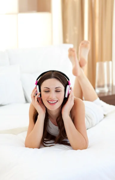 Brunette woman listening music lying on bed — Stock Photo, Image