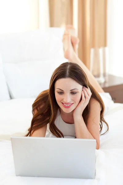 Завораживающая женщина смотрит на ноутбук, лежащий на кровати — стоковое фото