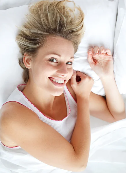 Piękna kobieta, leżąc w łóżku uśmiechając się do kamery — Zdjęcie stockowe