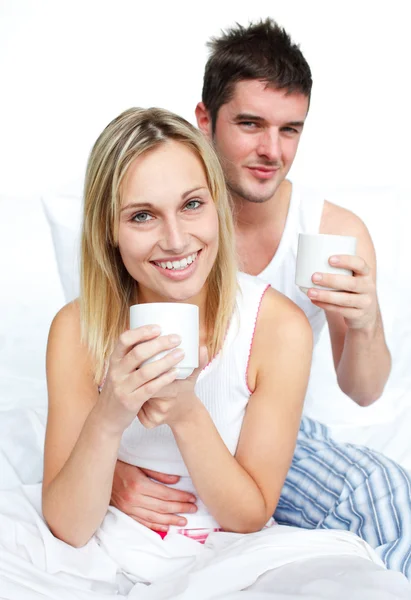 Para picia kawy w łóżku i uśmiechając się do kamery — Zdjęcie stockowe