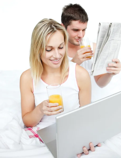 Couple reading a newspaper and using a laptop in bed — Stock Photo, Image