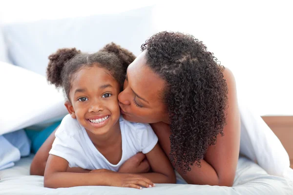 Loving woman kissing her daughter lying down on bed — Stock Photo, Image