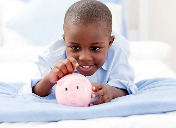 Νεαρό αγόρι σε ένα κρεβάτι βάζοντας χρήματα σε μια τράπεζα γουρουνάκι — Φωτογραφία Αρχείου