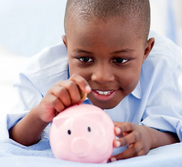 Jonge jongen op een bed geld steken in een piggy bank — Stockfoto