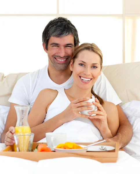 Smiling couple having breakfast lying in the bed — Stock Photo, Image
