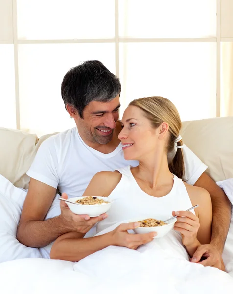 Cheerful lovers eating cereals lying in the bed — Stock Photo, Image