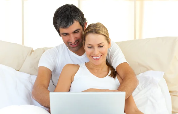 Förtjust par använder en bärbar dator i sängen — Stockfoto