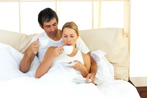 Casal alegre bebendo café deitado na cama — Fotografia de Stock
