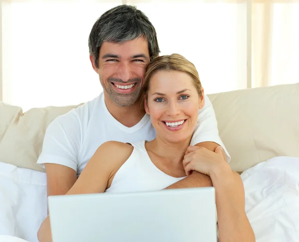 Sorrindo casal usando um laptop deitado na cama — Fotografia de Stock