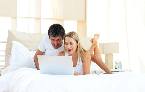 Joyful lovers using laptop lying on bed — Stock Photo, Image