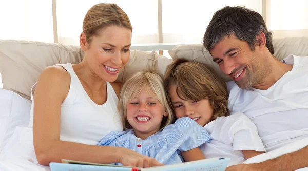 Familia alegre leyendo un libro en la cama —  Fotos de Stock