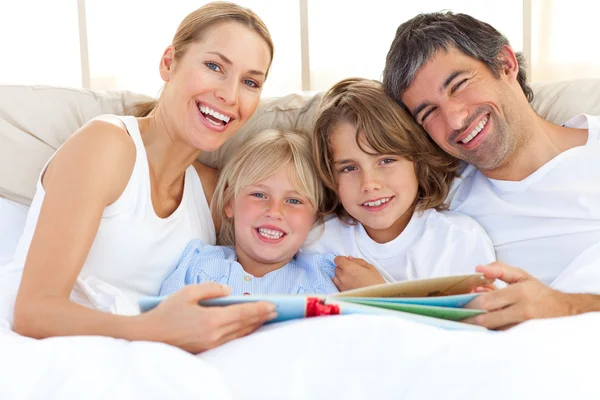 Lächelnde Familie liest ein Buch auf dem Bett — Stockfoto