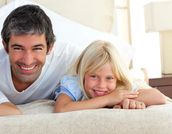 Усміхнена маленька дівчинка розважається зі своїм батьком, лежачи на ліжку — стокове фото