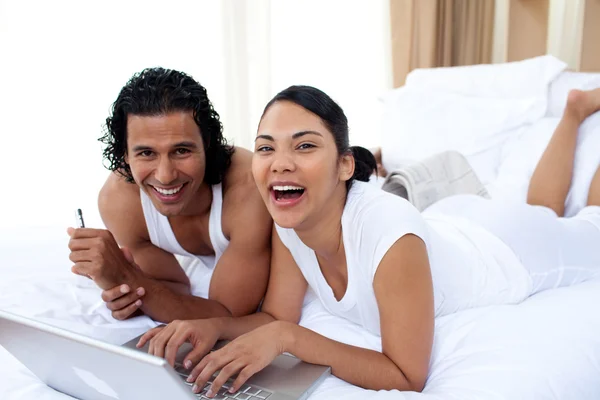 Casal usando um laptop deitado na cama — Fotografia de Stock