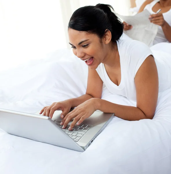 Donna felice utilizzando un computer portatile sdraiato sul letto — Foto Stock