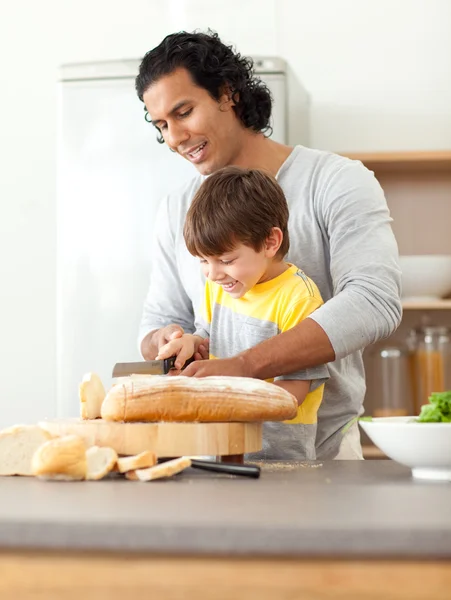 Внимательный отец помогает сыну порезать хлеб. — стоковое фото