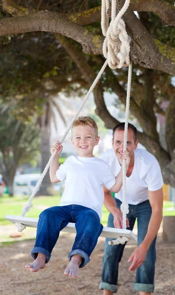Jolly father pushing his son on a swing — Stock Photo, Image