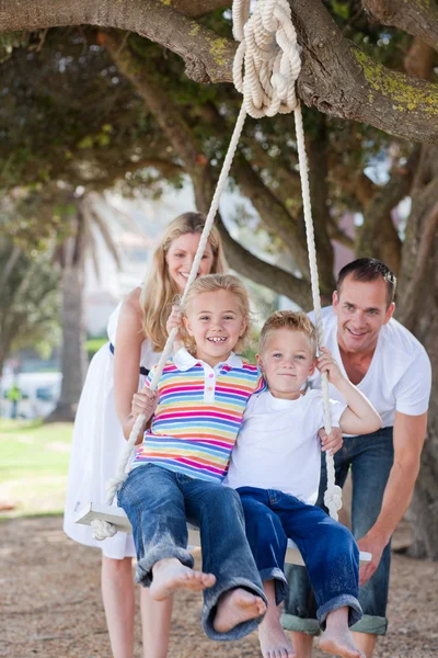 Happy parents pushing their children on a swing — Stock Photo, Image