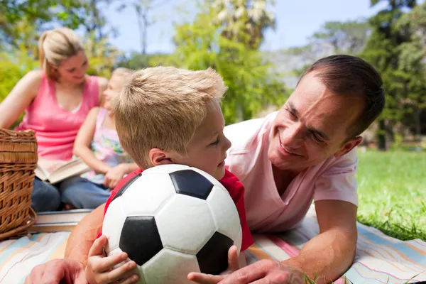 Father and son holding a soccer ball with their family reading i — Stock Photo, Image