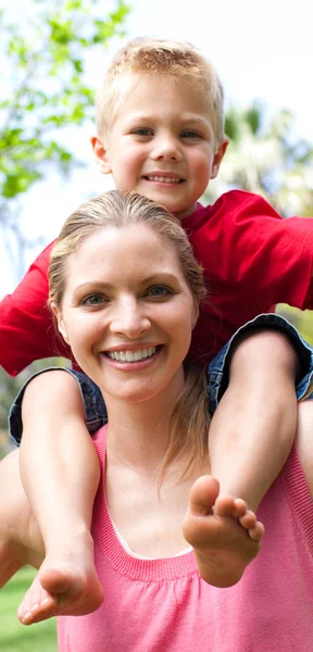 Närbild av en mamma som ger sin son en piggyback tur i en park — Stockfoto