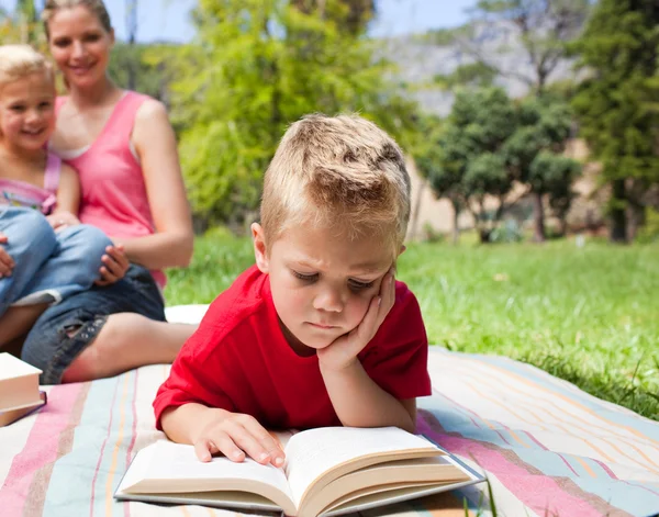 Menino sério lendo enquanto faz um piquenique com sua família — Fotografia de Stock