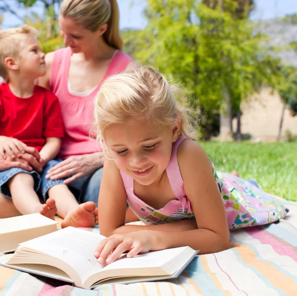 Skoncentrowany blond dziewczynka czytania podczas pikniku z jej f — Zdjęcie stockowe